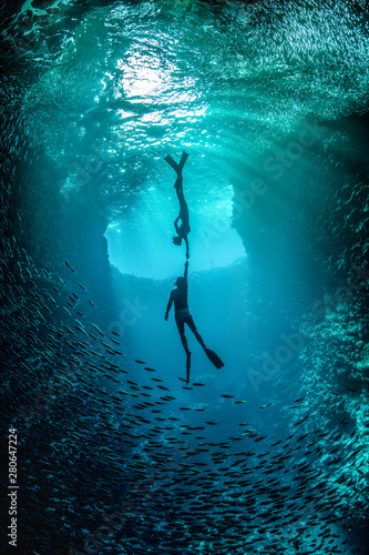 Free diving couple in love holding each others hand underwater in the cavern with back light