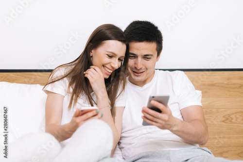 Happy laughing couple is watching media on smart phone sitting at home © dikushin