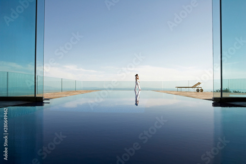 Woman talking on phone on patio with indoor / outdoor pool in foreground