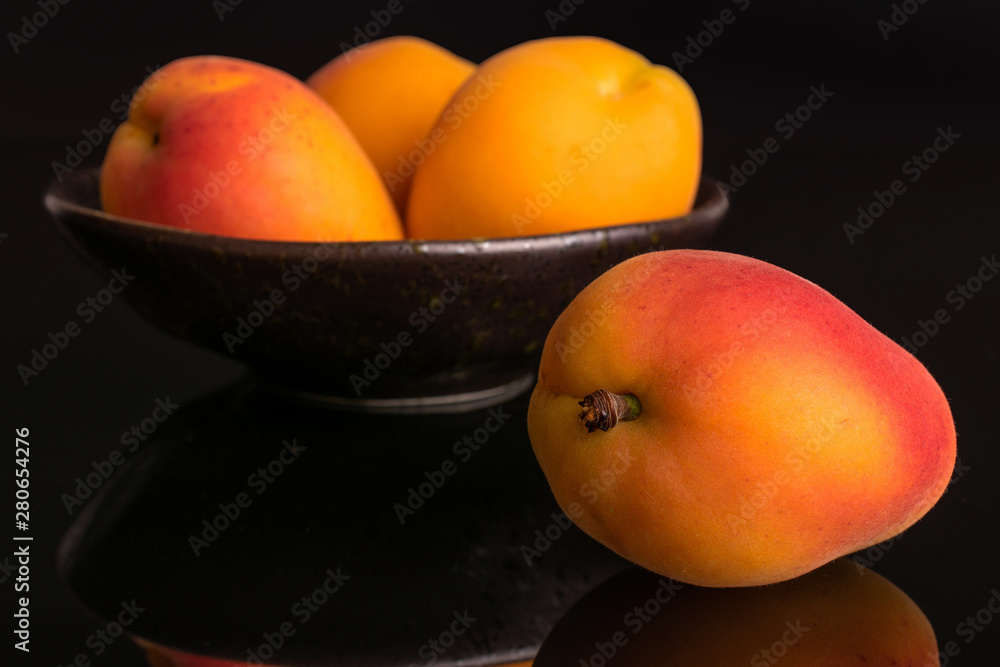 Group of four whole fresh orange apricot , one is in the front and the other three are in the back in a dark ceramic bowl isolated on black glass Group of four whole fresh orange apricot , one is in the front and the other three are in the back in a dark ceramic bowl isolated on black glass