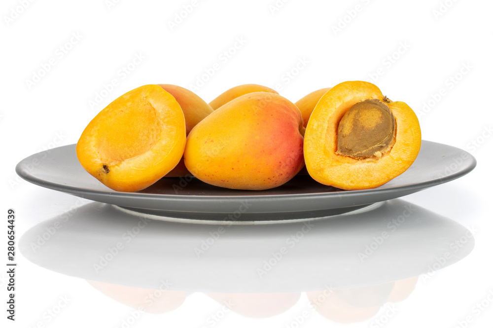 Group of four whole two halves of fresh orange apricot with an apricot stone on a gray ceramic plate isolated on white background