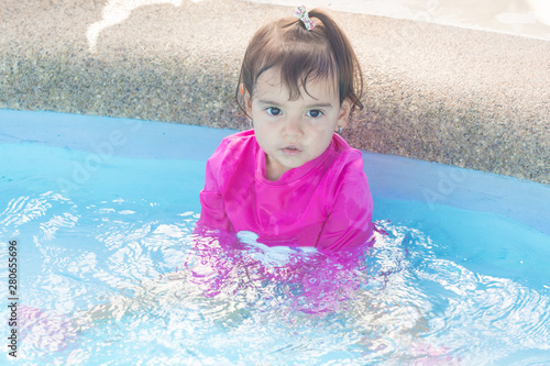 Baby girl of two years old splashes water in a swimming pool. She is happy and playful with her experience.