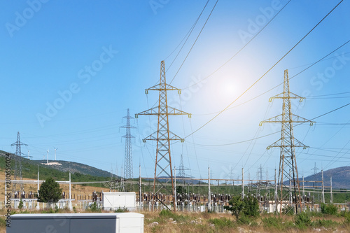 Electricity transmission pylons against blue sky. High voltage electricity poles with wind turbines.