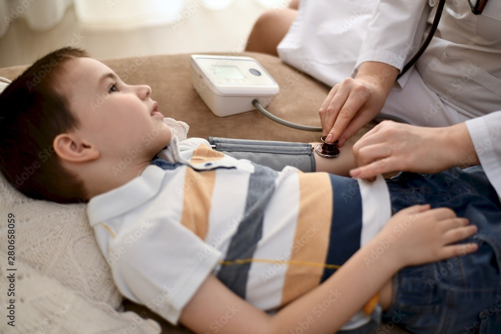 The boy lies on the bed and smiles, the doctor measures blood pressure with a tonometer. The boy lies on the bed and smiles, the doctor measures blood pressure with a tonometer.