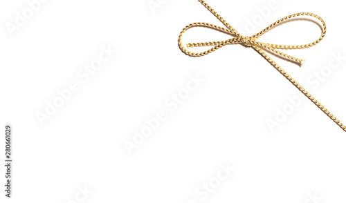 Golden satin rope upper right corner with knotted bow gift ribbon wrap for Christmas present with intricate shine details isolated cut out top view on simple plain wide banner white background.