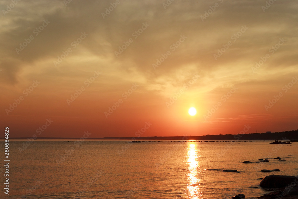 Scenic sunset over the sea. Reflection of the sun in water. The sky is painted with bright colors. Sunset beach in a summer evening. Gulf of Finland, Baltic sea,  Komarovo, Saint-Petersburg, Russia.