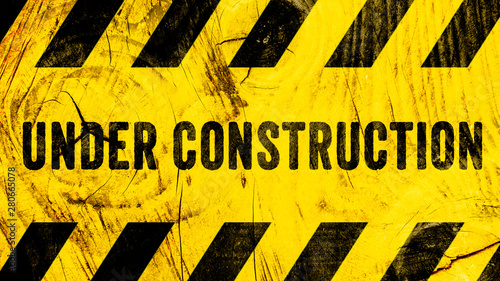 Under construction warning sign text with yellow black stripes painted on wood wall plank texture wide banner panorama background. Concept do not enter the area, caution, danger, construction site.