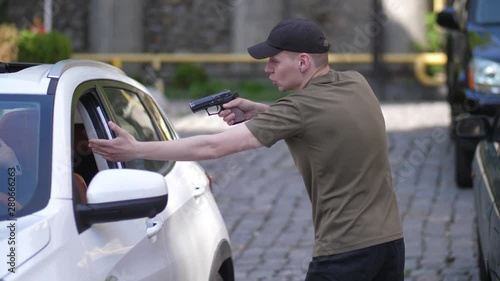 Side view of aggressive criminal threatening man driving car with pistol through open window. Fearless driver snatching gun and punching thug extorting keys to hijack car in the middle of day
