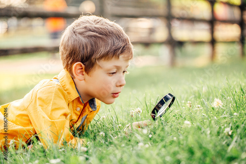 Cute adorable Caucasian boy looking at plants grass in park through magnifying glass. Kid with loupe studying learning nature outside. Child natural science education concept. photo