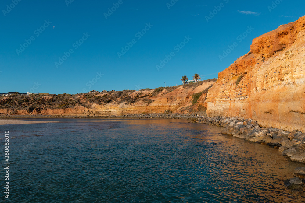 Beach coastline with rock cliff and deep blue sky.