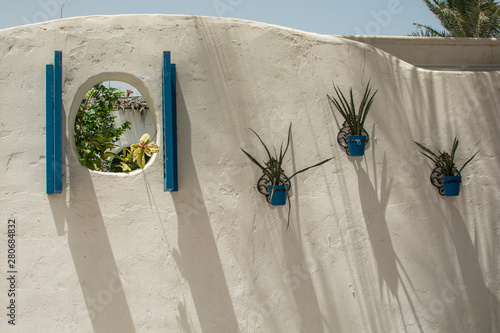 Fototapeta Naklejka Na Ścianę i Meble -  White street wall with green plants in blue pots in greece