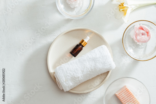Top view of Spa products with towel and oil on plate, flowers, soap on white background