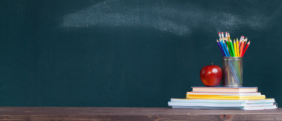Pencil tray and an apple on notebooks on school teacher's desk.