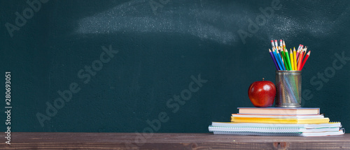 Pencil tray and an apple on notebooks on school teacher's desk.