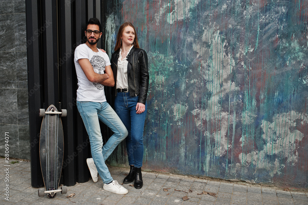 Cool multiracial couple posing against wall with longboard. Cool multiracial couple posing against wall with longboard.