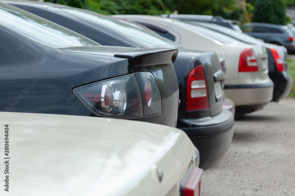 Row of cars and vans parked in parking lot during the daytime. The back of the trunk is visible in the parking space on blurred background. Transportation and parking.
