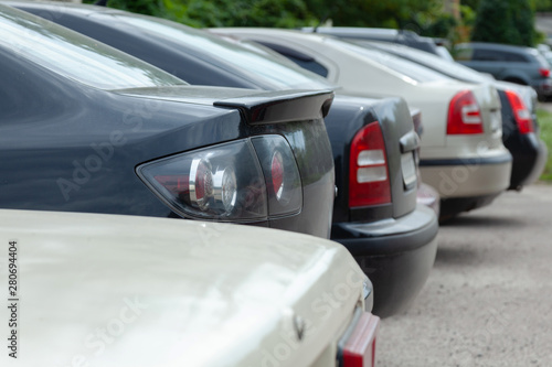 Row of cars and vans parked in parking lot during the daytime. The back of the trunk is visible in the parking space on blurred background. Transportation and parking.