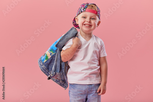 Little serious fashionable toddler boy in denim clothes and trendy cap. Isolated on pink background