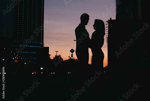 Silhouette of young happy couple in love kissing on city street at sunset
