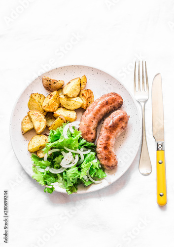 Roasted turkey sausages with baked potatoes and green salad - delicious lunch, snack, tapas on a light background, top view