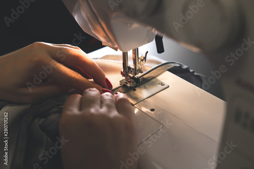 Fototapeta Naklejka Na Ścianę i Meble -  Woman is working at sewing machine. Girls hands with red manicure. Fashion concept. Creating of new clothes process. Hobby ideas.