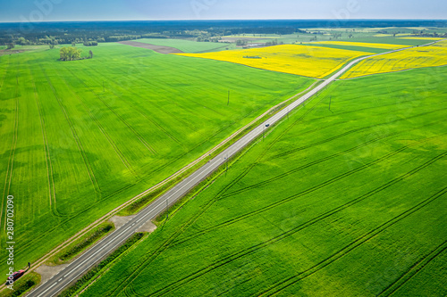 Moving cars on a road between green fields, aerial view