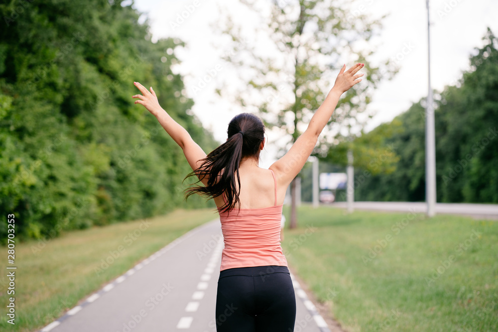 Happy woman celebrating rising hands to the sky on the road. Female sportsman expressing positivity and success. Freedom, confidence, motivation Happy woman celebrating rising hands to the sky on the road. Female sportsman expressing positivity and success. Freedom, confidence, motivation