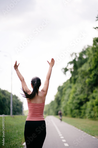 Happy woman celebrating rising hands to the sky on the road. Female sportsman expressing positivity and success. Freedom, confidence, motivation