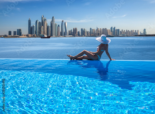 Canvas Print Beautiful panorama of Dubai Marina skyline in a background with a pool, deck chair and woman with a white hat