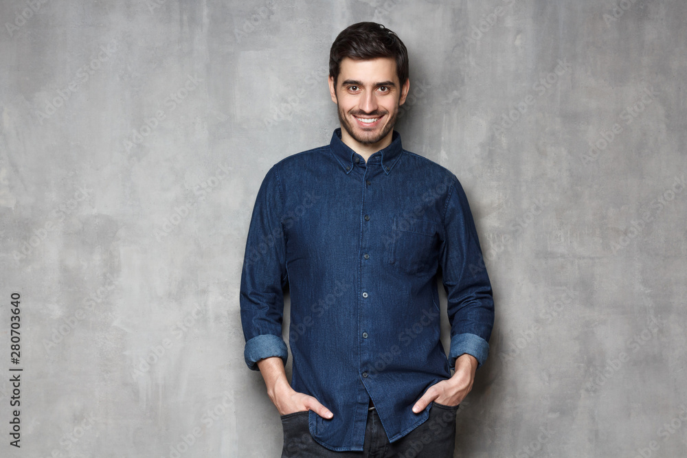 Young handsome man standing against gray wall