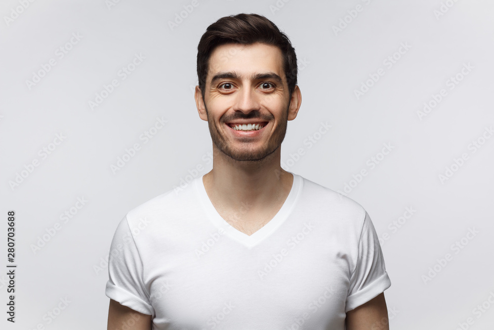Handsome smiling young man in casual white t-shirt, looking at camera, isolated on gray background Handsome smiling young man in casual white t-shirt, looking at camera, isolated on gray background