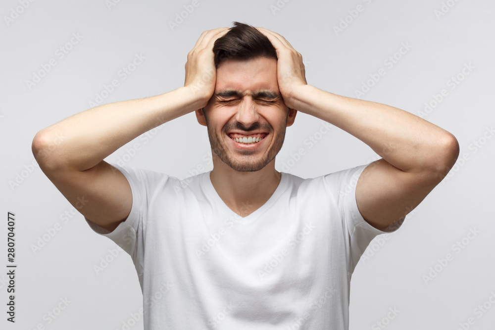 Young man pressing hands to temples experiencing bad headache, having shut eyes because of pain, isolated on gray background Young man pressing hands to temples experiencing bad headache, having shut eyes because of pain, isolated on gray background