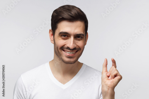 фотографія Young man with shows something tiny, smiling isolated on gray background