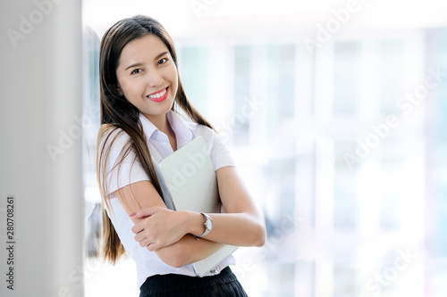 Free Download Portrait of young student smiling and holding tablet while standing in classroom. - GFXLoad