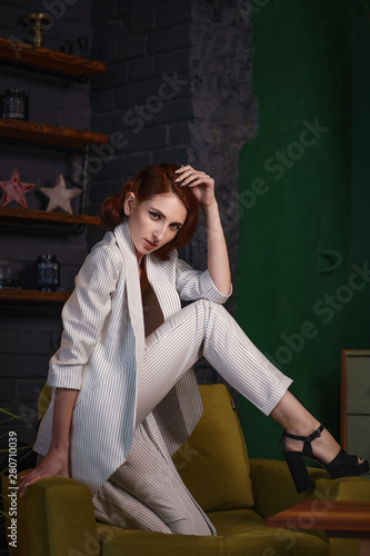 Concept: fashion, beauty. Pretty redhead thin lean young woman with vintage hairdo alluring in white unbuttoned pant suit. Studio photoshoot.