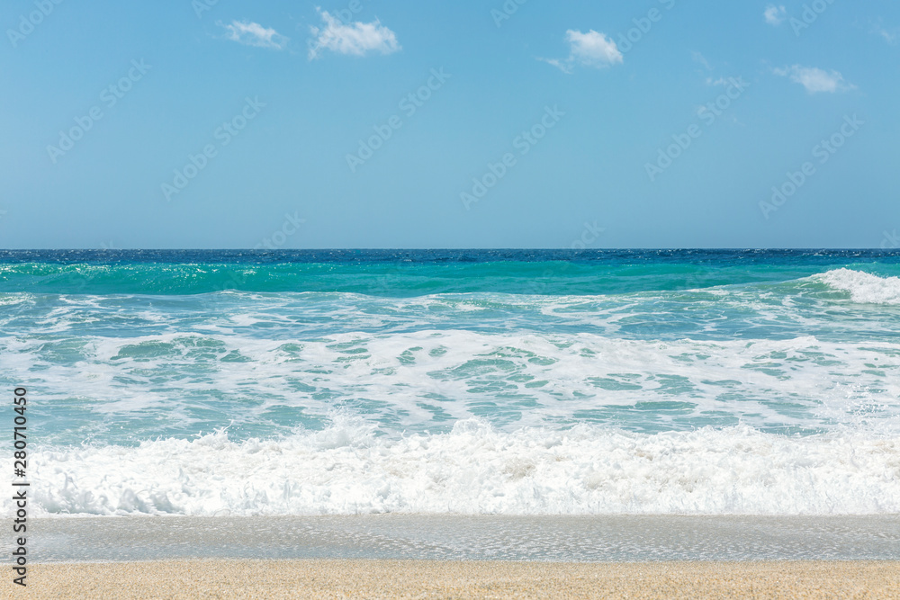 Sandy coast of the turquoise sea. Surging waves, sunny windy day. Space for text.