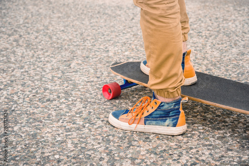 Close-up of male legs in rag sneakers on a longboard on the background of asphalt at sunset. Big skateboard with man legs. Youth leisure concept