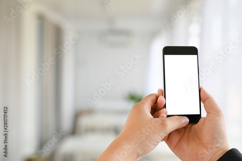Man's hands using mockup mobile phone with empty screen in living room. © Prathankarnpap