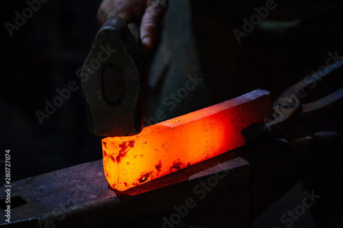 The blacksmith manually forging the red-hot metal on the anvil in smithy