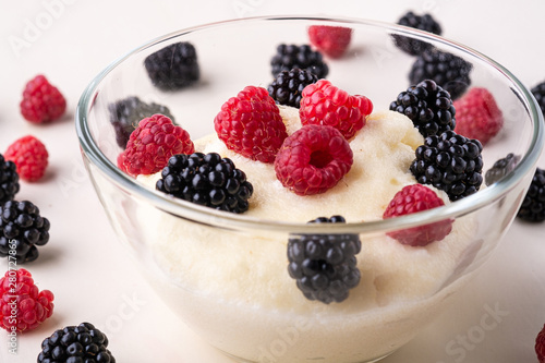 Semolina pudding porridge dessert with blackberry and raspberry in glass bowl near with scattered heap in order berries on white wooden background, breakfast, isolated, selective focus