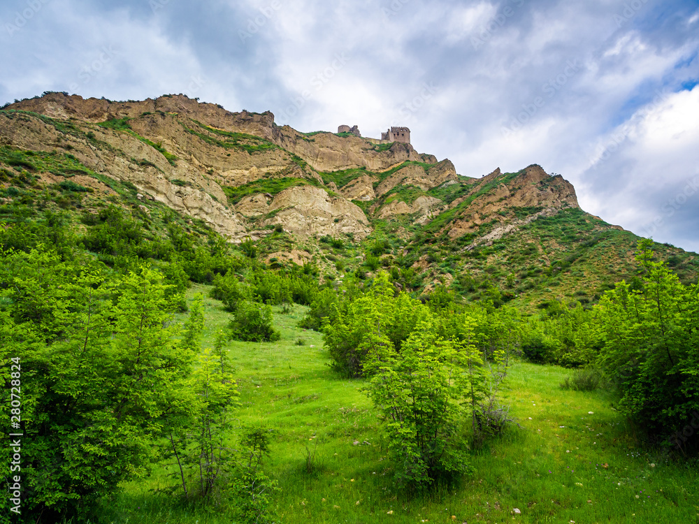 Bottom view of a cliff with old Georgian Ksani fortress at its top