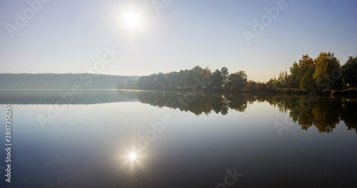 Panorama with bright sun reflected in the water of the lake. Calm on the lake. © vladk213