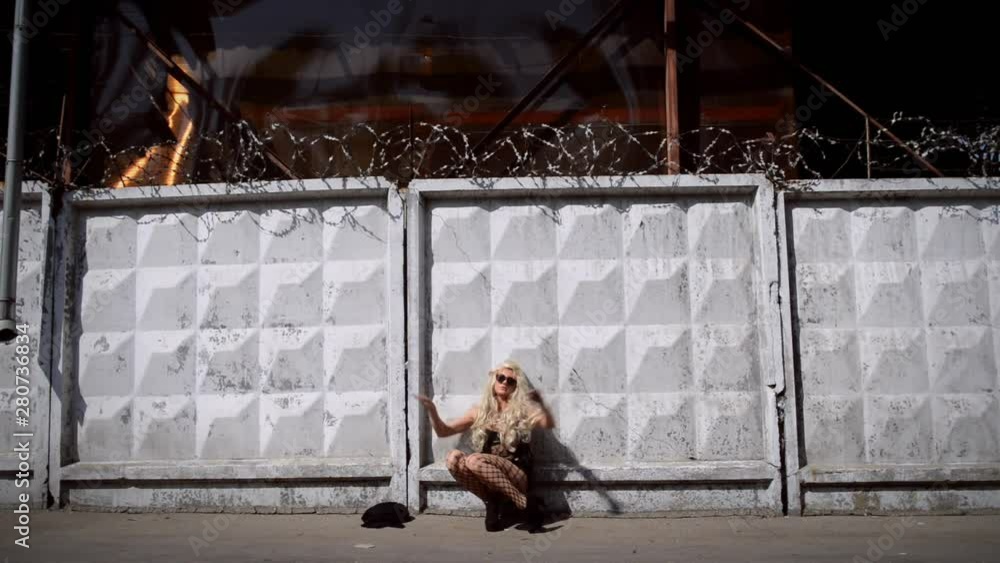 Young freaky woman in black dress and stockings sits on background of white fence with barbed wire in day time. Video concept restriction of freedoms in Russia Young freaky woman in black dress and stockings sits on background of white fence with barbed wire in day time. Video concept restriction of freedoms in Russia