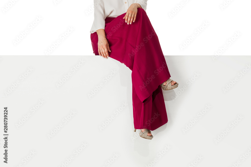 beautiful legs woman wearing burgundy trousers and high heels shoes sitting on white bench.