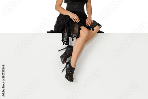 Beautiful legs woman wearing black dress and high heels shoes sitting on white bench. with copyspace.