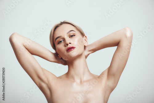 Freshness. Young healthy woman holding her arms up and showing clean underarms while standing against grey background photo