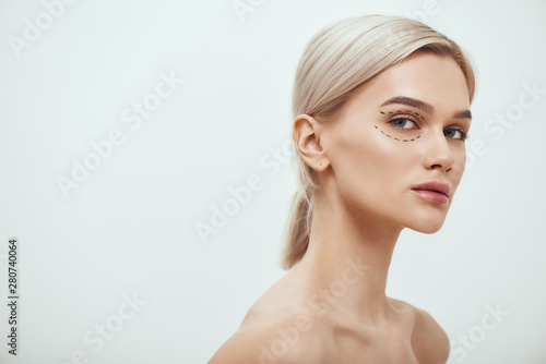 Perfection. Beautiful and young blonde woman with black surgical lines on eyelids and under eyes looking at camera photo