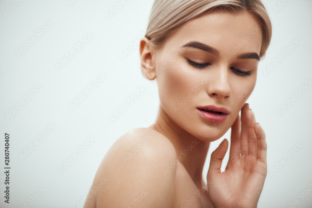 Naklejka premium I love my skin. Attractive young blonde woman keeping eyes closed and touching her face while standing against grey background
