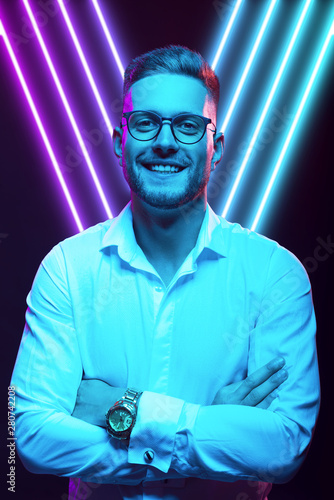 Young handsome model posing in a studio in a trendy neon light. Fashionable man in a stylish suit. Vibrant color. Bright colorful light effects. Disco style. Overlay. Gel filter. Supersaturated