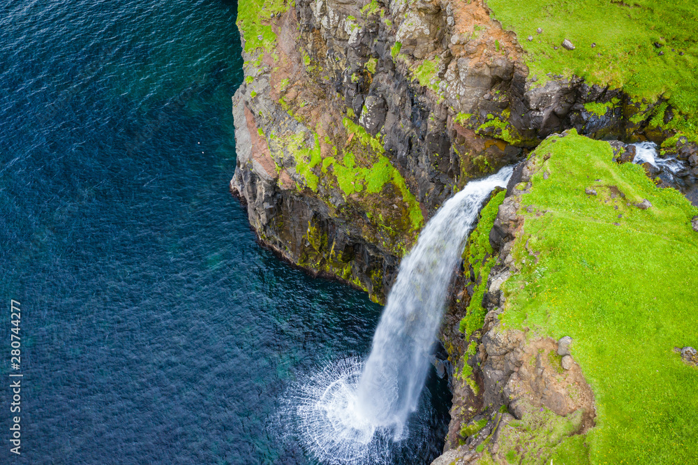 Aerial view of Mulafossur waterfall in Gasadalur village in Faroe Islands, North Atlantic Ocean. Photo made by drone from above. Nordic Natural Landscape.